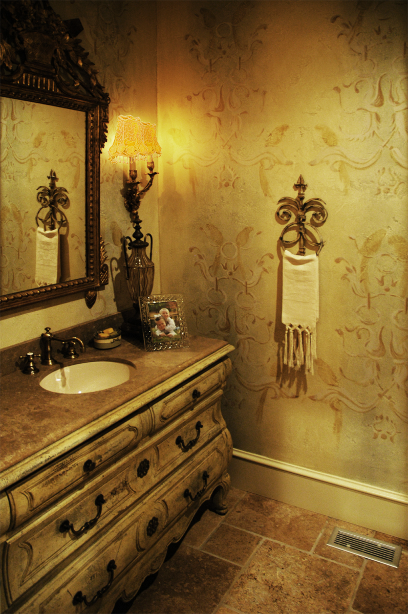 Guest Bath Makeover – Done in tone on tone custom free-hand wall pattern design over a custom colored base coat is the perfect complement to the facsimile vanity piece and stone flooring.